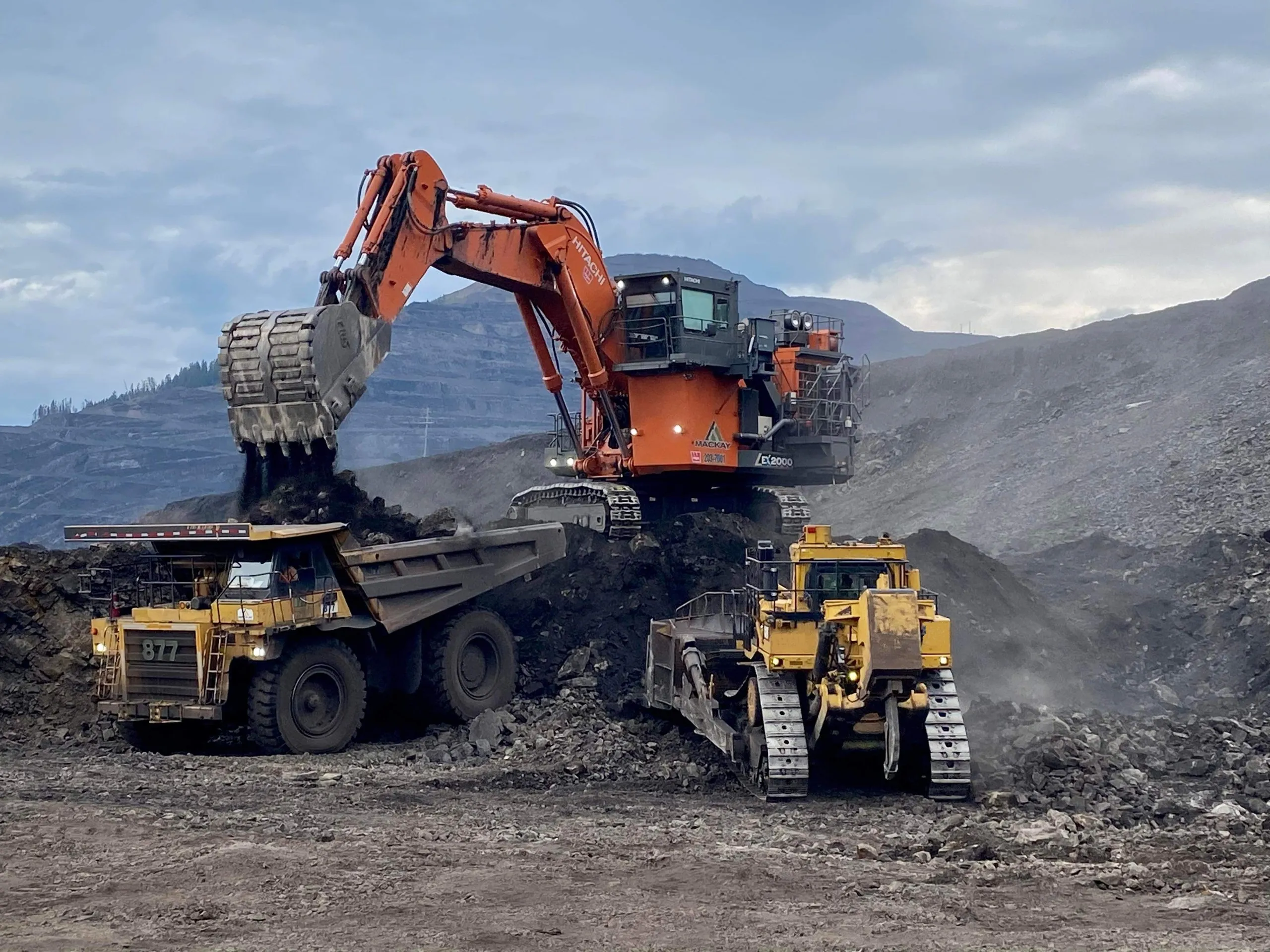 Excavator loading haul trucks on an active mine bench under a dramatic sky